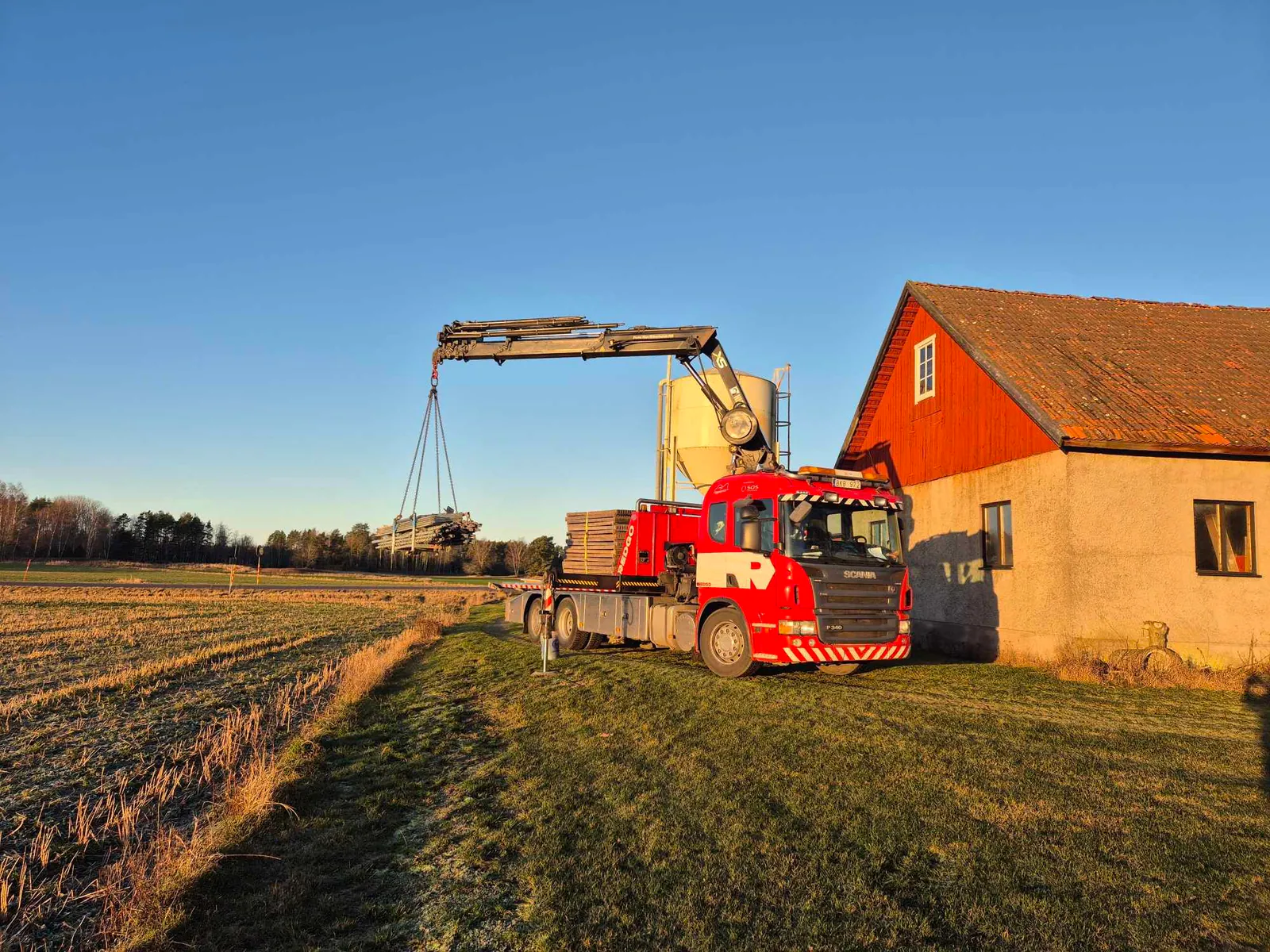 Götenebärgarens kranbil lyfter en bunt material vid en gård